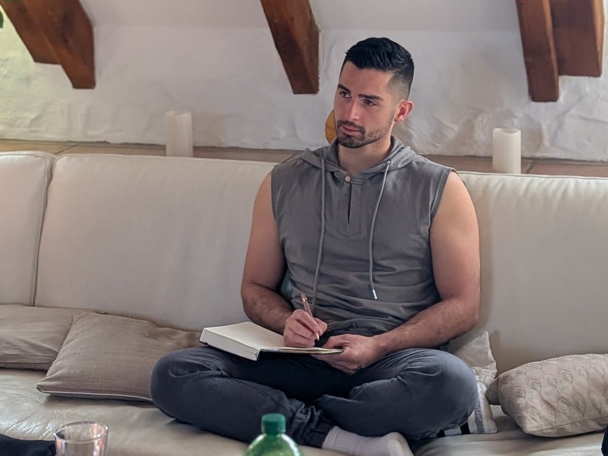 Ein Teilnehmer sitzt im Schneidersitz auf dem Sofa, schreibt in sein Notizbuch und blickt nachdenklich zur Seite